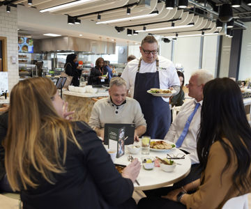 A group of employees being served food by a member of the 14forty catering team in a workplace canteen.